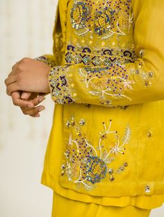 Editor's Note Mustard Hand Embroidered Jacket With Matching Peplum And Sharara In Crepe Fabric: Crepe, Organaza Color: Mustard Care: Dry Clean Only About the Designer Sanya Gulati's designs are inspired by the Indian bridesmaids, pastel easy hues & seasonal trends, her designs are a mix of modern, contemporary embroideries with traditional silhouettes thus creating our signature asymmetric checks embroideries amalgamated with floral thread work, through her designs, the designer aims to enhance Yellow Long Sleeve Top With Resham Embroidery, Yellow Kurta With Floral Embroidery And Long Sleeves, Yellow Long Sleeve Kurta With Floral Embroidery, Spring Traditional Wear With Multicolor Embroidery And Long Sleeves, Yellow Long Sleeve Top With Chikankari Embroidery, Yellow Long Sleeve Blouse With Resham Embroidery, Spring Embroidered Long Sleeve Bandhgala, Festive Yellow Long Sleeve Tops, Long Sleeve Blouse With Dabka Work For Festive Occasions