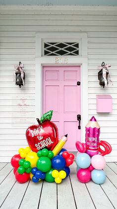 an apple sits on top of balloons in front of a pink door that says happy school