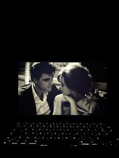 a black and white photo of a couple kissing in front of a laptop computer screen