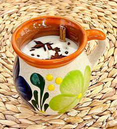 an orange and white cup filled with milk sitting on top of a woven table cloth