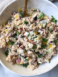 a white bowl filled with chicken salad on top of a table next to a wooden spoon