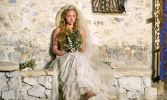 a woman in a wedding dress sitting on a stone wall with flowers and greenery