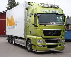 a green semi truck parked in front of a red and white building with an orange sign on it's side