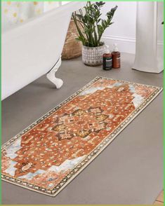 an orange rug is on the floor next to a bathtub and potted plant