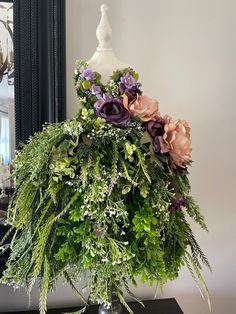 a vase filled with flowers and greenery sitting on top of a table next to a mirror