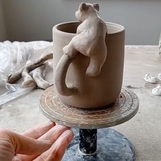 a hand is holding a clay cup with a bear on it