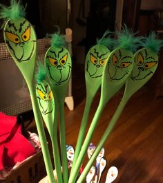 four green plastic spoons with faces painted on them in a vase filled with toothbrushes