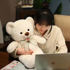 a woman sitting in front of a laptop computer holding a teddy bear