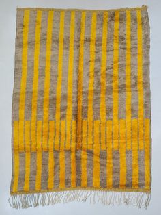 a yellow and grey striped rug with fringes on it's edges, against a white background