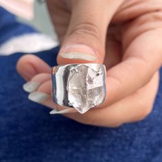 a woman's hand holding a ring with a large diamond in it, on top of a blue surface