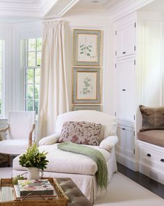 a living room with white furniture and paintings hanging on the wall above it's windows