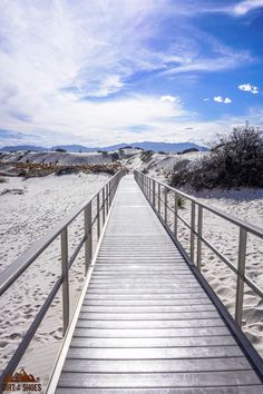 a wooden walkway leading to the beach with white sand and blue skies in the background