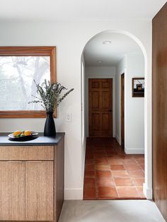 an archway leading to a kitchen with tile flooring and wooden cabinetry, along with a bowl of fruit on the counter