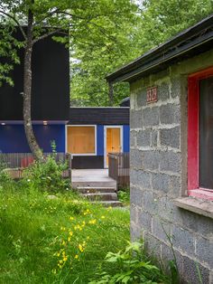 two houses in the woods with trees and grass around them, one has red door