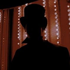 the silhouette of a man wearing a top hat in front of a window with beads