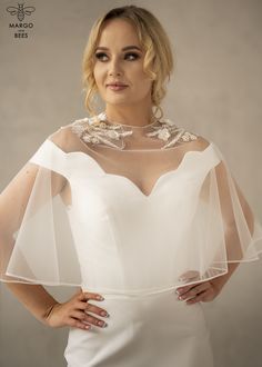 a woman wearing a white dress with sheer sleeves and beaded neckline is posing for the camera