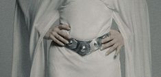 a woman with her hands on her hips wearing a white dress and holding a silver belt