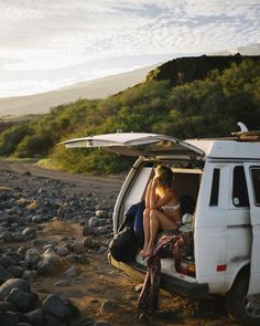 a woman sitting in the back of a white van on top of a rocky beach