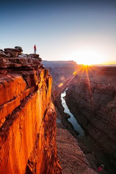 the sun is setting at the edge of a cliff overlooking a river and canyon below