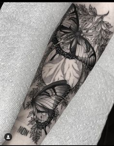 a black and white tattoo with two butterflies on the left arm, surrounded by leaves