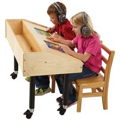 two children are sitting at a table with headphones on and one child is reading