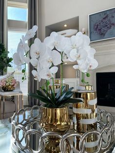 white flowers are in gold vases on a mirrored coffee table with candlestick holders