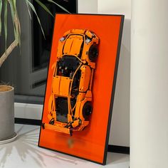 an orange toy car is on display in front of a potted plant