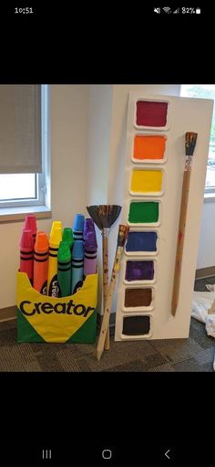 there are many crayons on the floor next to some paintbrushes and an easel