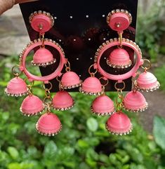 a pair of pink and gold earrings hanging from a green plant in front of a black background