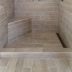 a walk in shower sitting next to a tiled wall and floor covered in brown tile