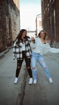 two women standing in an alley with one holding the other's hand and smiling