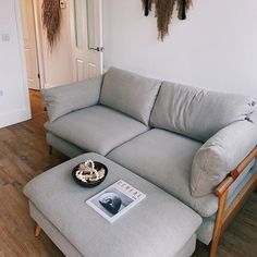 a couch and ottoman in a room with wood floors, white walls and wooden flooring