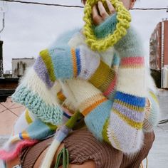 a woman sitting on the back of a motorcycle talking on a cell phone while wearing a multicolored sweater