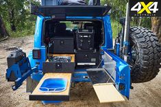 the back end of a blue truck with its doors open on dirt road next to trees