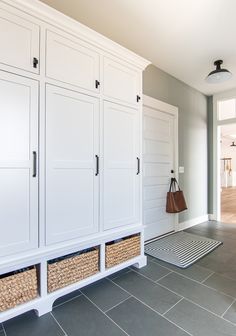 an entryway with white cabinets and baskets on the floor