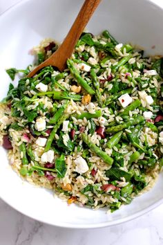 a white bowl filled with rice, asparagus and feta cheese next to a wooden spoon