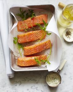 four salmon fillets in a baking pan with herbs and seasoning on the side