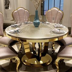 a round dining table with beige chairs and gold trimmings is surrounded by white walls