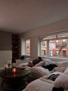 a man laying on top of a white couch in a living room next to a window