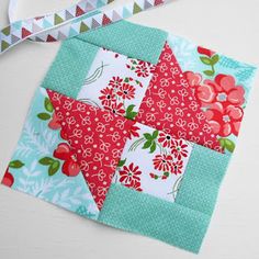 a red and blue patchwork piece with flowers on it next to a pair of scissors