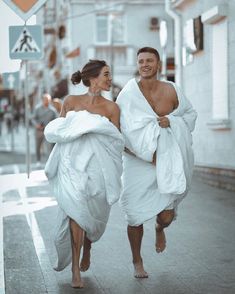 two people wrapped in white towels running down the street with one person holding his arm around the other