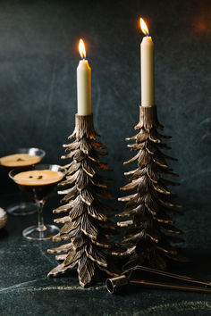 two candles sitting next to each other on top of a black table with wine glasses