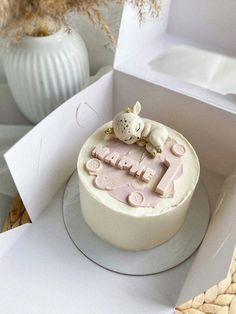 a white cake with pink frosting sitting in a box next to a flower vase