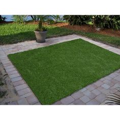 a green grass area in the middle of a brick walkway with potted plants next to it