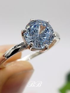 a close up of a person holding a ring with a blue diamond in the center