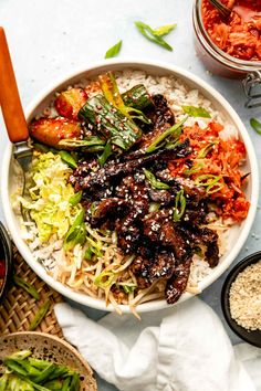 a bowl filled with meat and vegetables on top of rice next to bowls of sauce