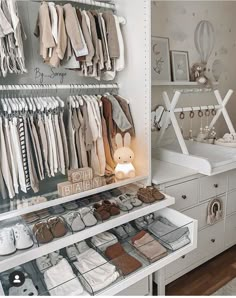 a white closet filled with lots of baby clothes and shoes on shelves next to a dresser