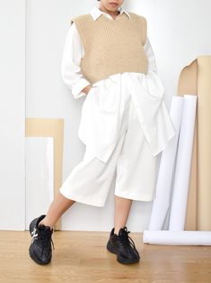 a young boy standing in front of a white wall wearing black shoes and a sweater