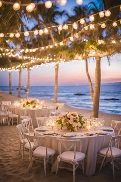 an outdoor dinner setup on the beach with lights strung over it and candles lit up