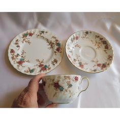 three antique tea cups and saucers, one with flowers on the rim is being held by a person's hand